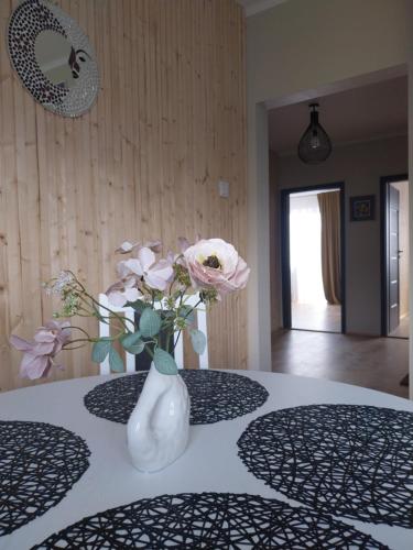 a white vase with flowers sitting on a table at Saulės miesto apartamentai in Šiauliai