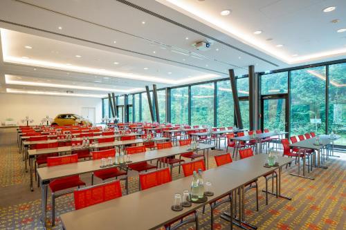 a restaurant with tables and red chairs and windows at Holiday Inn Munich - Westpark by IHG in Munich