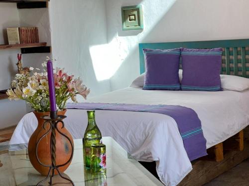 a bed with purple pillows and a vase with flowers on a table at Hacienda Santa Barbara Casa Malinche in Huamantla