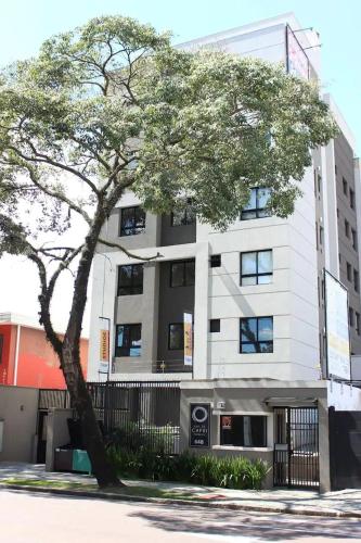 a tall white building with a tree in front of it at CPR26 - Studio Com Arquitetura Industrial no Juvevê- Curitiba in Curitiba