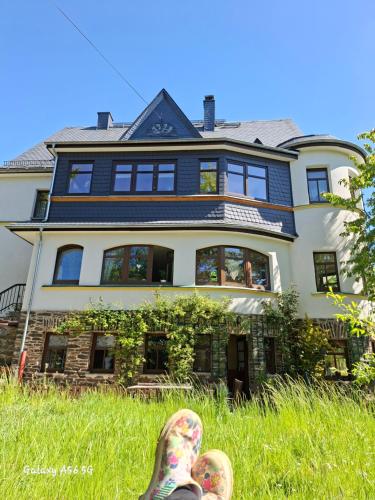 a person with their feet up in the grass in front of a house at ansimali 1- Gemütliche FeWo mit Küche und Gartenblick in Grünhain-Beierfeld für Tierfreunde und Radliebhaber in Grünhain-Beierfeld