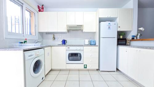 a white kitchen with a refrigerator and a dishwasher at CSS Cheerful Smart Superior 2BD Townhouse Limnaria Gardens in Paphos City