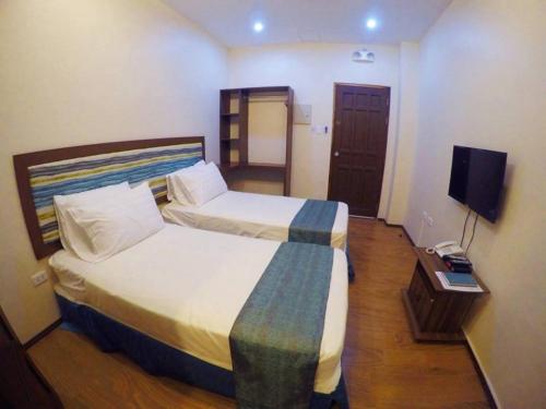 a hotel room with two beds and a flat screen tv at Golden Gate Suites in Dumaguete