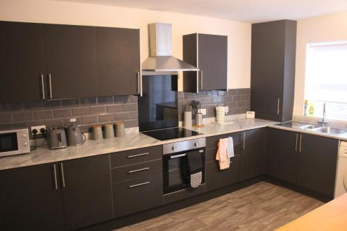 a kitchen with black cabinets and stainless steel appliances at Tastefully furnished and Cosy 2-bedroom house in South Shields