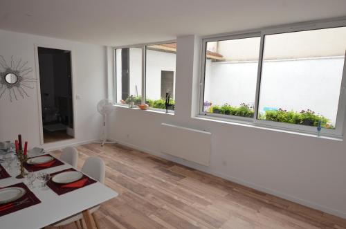 un salon blanc avec une table et deux fenêtres dans l'établissement Appartement Cordier, à Saint-Amand-Montrond