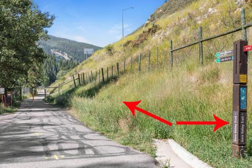 a road with two arrows in the grass next to a fence at Private Hot Tub Overlooking Gore Creek, Parking for 4, Updated Townhome in Vail