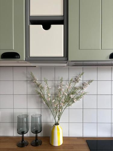 a yellow vase with flowers in it next to two glasses at Dębina Lounge 20 Apartamenty in Debina