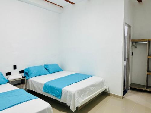 two beds in a white room with blue sheets at Amanecer Santorini in Estación El Salto