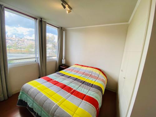 a small bedroom with a colorful bed in front of a window at Departamento Alto Libertad Meseta Coraceros in Viña del Mar
