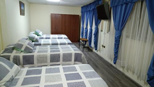 two beds in a room with blue curtains and a television at Hotel las Dunas in Iquique