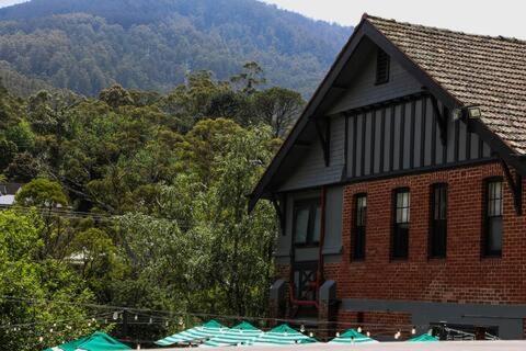 a large brick house with a mountain in the background at Alpine Hotel, Eat Drink Sleep in Warburton