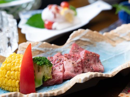 a plate of food with corn on the cob and meat at Livemax Resort Yuhigaura Kitu Onsen in Kyotango
