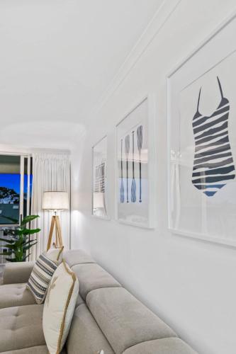 a white living room with a couch and pictures on the wall at Palm & Sea Trinity Beach in Trinity Beach