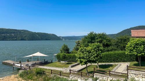 a view of a lake with a bench and an umbrella at Pensiunea Casa Mircea & Restaurant in Eşelniţa