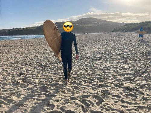 a person walking on the beach with a surfboard at Teach Chnoc na hEorna in Goleen