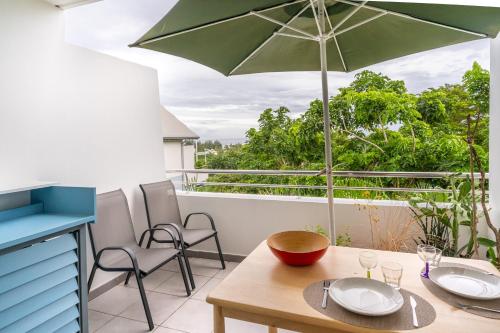 a balcony with a table and a green umbrella at FLAMBOYANT - Studio 2 personnes avec lit de qualité hôtelière séparable pour couple ou amis avec très belle terrasse à 12 min à pied ou 4 min en voiture du lagon de l'Ermitage - ST GILLES LES BAINS in La Saline les Bains