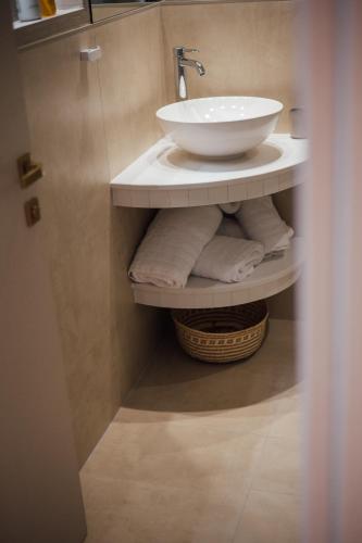 a bathroom with a white sink and towels on a shelf at Parga Harbor Suites in Parga