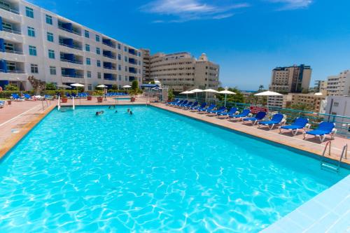 a large swimming pool with blue chairs and buildings at Apartamentos Tamaragua in Playa del Ingles