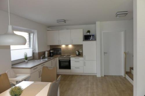 a kitchen with white cabinets and a table with a dining room at 6 Personen Ferienhaus mit Sauna, Whirlpool, zwei Duschen sowie Kaminofen in Otterndorf in Otterndorf