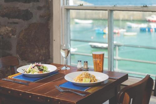 einen Tisch mit zwei Teller Essen und einem Glas Wein in der Unterkunft The Ship Inn in Mousehole