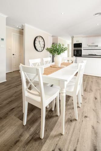 a white dining room table with white chairs and a clock at Summery 4BR Home by Mel Airport, CBD & Watergardens in Sydenham