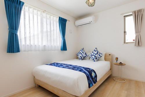 a white bedroom with blue curtains and a bed at 那覇空港から15分DMM水族館とイーアス豊崎近く最大10名oKの南部リゾート宿OKS inn in Itoman