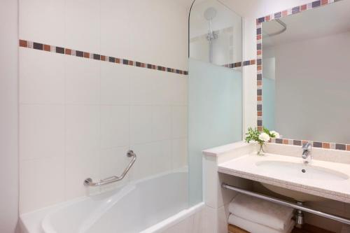 une salle de bain blanche avec une baignoire et un lavabo dans l'établissement Fraser Suites Paris La Défense, à Courbevoie