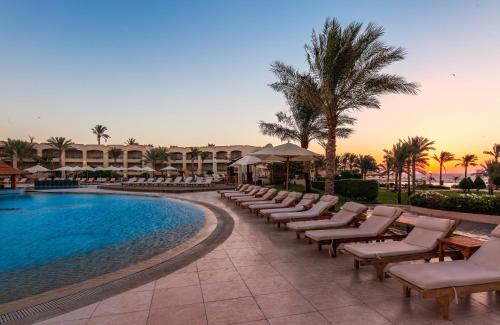 un complexe avec piscine, chaises et palmiers dans l'établissement Cleopatra Luxury Resort Sharm El Sheikh, à Charm el-Cheikh