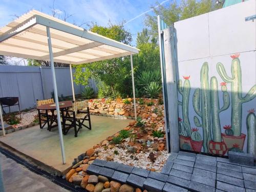 a patio with a table and a fence with a cactus mural at Karoo Nest - Calitzdorp in Calitzdorp