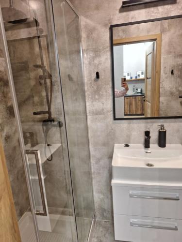 a bathroom with a shower and a sink and a mirror at Apartamenty MILANHOUSE in Gołdap
