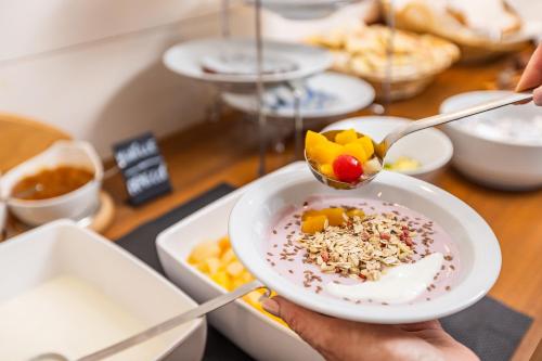 a person holding a bowl of food with a spoon at Hotel Heide Park in Ora/Auer
