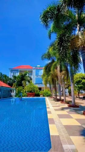 a swimming pool with palm trees in front of a building at Ven Song Riverside Hotel in Ho Tram