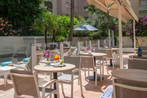a patio with tables and chairs and an umbrella at Hotel Amarante Cannes in Cannes
