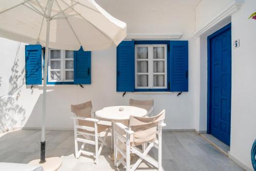 a white table and chairs with blue windows and an umbrella at Maroulis Studios Naxos in Mikri Vigla