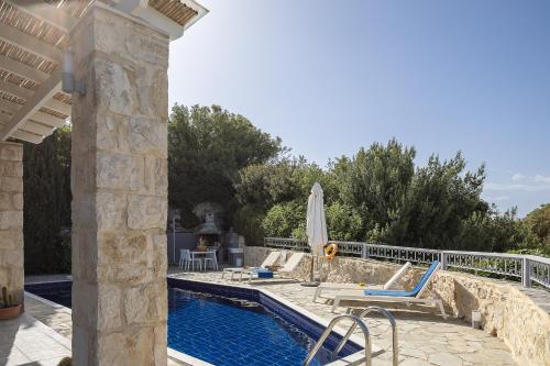 a swimming pool with chairs and a umbrella on a house at Villa Ikaros in Agia Triada