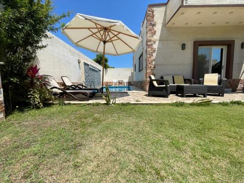 a patio with an umbrella and chairs and a pool at Nubian Villa with Private Pool in Naj‘ al Aḩwāl