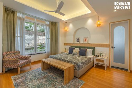 a bedroom with a bed and a chair and a window at StayVista at The Ever House with Bonfire, Jacuzzi, Bathtub in Dharampur