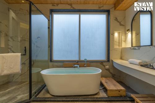 a bath tub in a bathroom with a window at StayVista at The Ever House with Bonfire, Jacuzzi, Bathtub in Dharampur