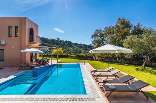 a pool with chairs and umbrellas next to a house at Villa Ithaki Kefalonia in Lourdhata
