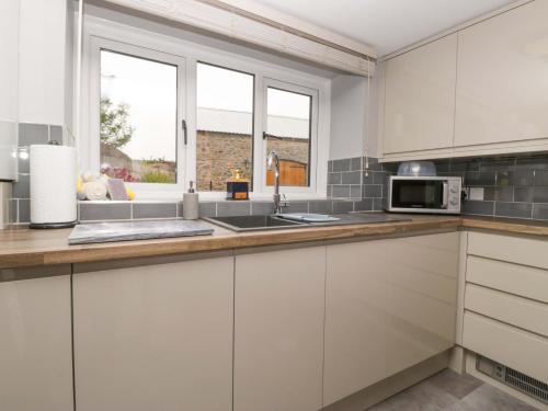 a kitchen with white cabinets and a sink at Yeat Stoup Cottage in Cockermouth