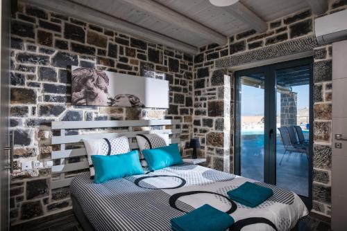 sypialnia z kamiennymi ścianami i łóżkiem z niebieskimi poduszkami w obiekcie Anna Luxury Villa Cretevasion w mieście Kokkini Hani