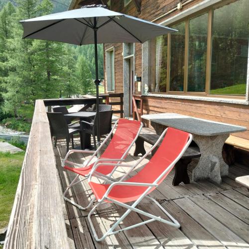 two chairs and a table with an umbrella on a deck at La Piana Appartamenti in Alpe Devero