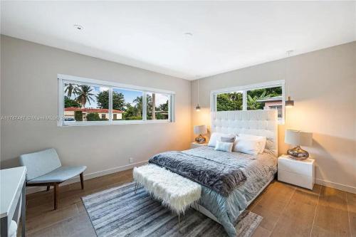 a bedroom with a bed and a chair and two windows at Miami Shores Modernist Villa in Miami Shores