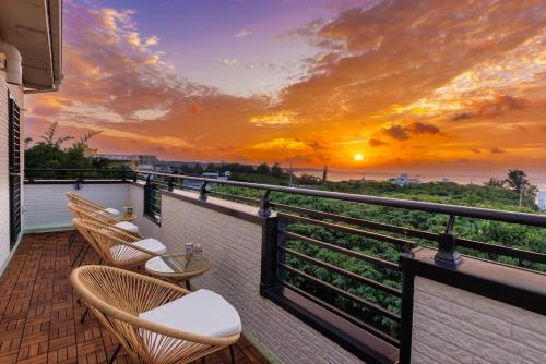a balcony with chairs and a sunset over the ocean at Maeda Reaf Resotプライベートビーチまで徒歩3分 in Onna