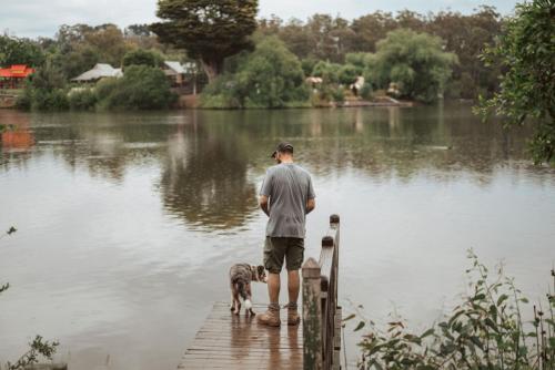 a man standing on a dock with a dog on a lake at Romantic Lakefront Luxury - Spa Bath, Fireplace, King Bed in Daylesford