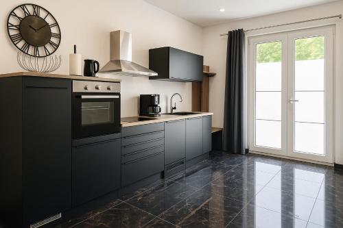 a kitchen with black cabinets and a clock on the wall at Werre Apartments mit Smart-TV - stilvol, zentral & wohnlich in Löhne