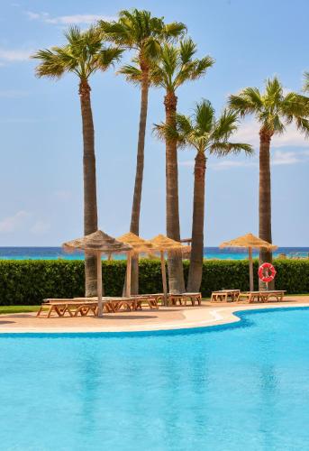 a swimming pool with palm trees and umbrellas at Sol Milanos Pingüinos in Son Bou