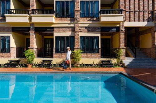 a woman walking by a pool in front of a building at Motive Cottage Resort in Khao Lak