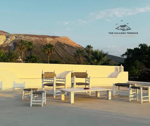 a group of tables and chairs next to a yellow wall at The Vulcano Terrace in Vulcano