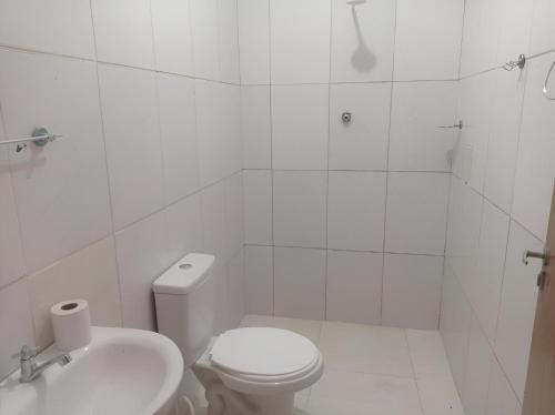 a white bathroom with a toilet and a sink at Pousada Sinai in Viçosa
